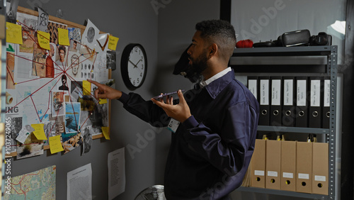 African american detective analyzing clues on wall board while recording voice note in office photo