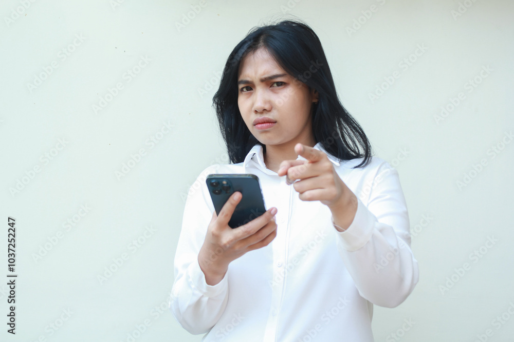 portrait of sad unbelieve asian business woman pointing to camera with glare eye holding smartphone, disappointment and disatisfied expression, wear formal white suit standing over isolated background portrait of sad unbelieve asian business woman pointing to camera with glare eye holding smartphone, disappointment and disatisfied expression, wear formal white suit standing over isolated background