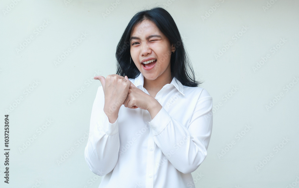 studio shot of excited asian young business woman pointing to side empty space with her thumbs look at camera flirting blink eye wearing white formal suit shirt isolated on white background studio shot of excited asian young business woman pointing to side empty space with her thumbs look at camera flirting blink eye wearing white formal suit shirt isolated on white background