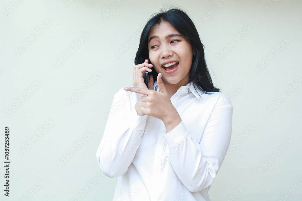 portrait of success asian young business woman manager speaking on smartphone with excitement look aside pointing finger beside to empty space with thumbs up wearing white formal suit shirt, standing portrait of success asian young business woman manager speaking on smartphone with excitement look aside pointing finger beside to empty space with thumbs up wearing white formal suit shirt, standing