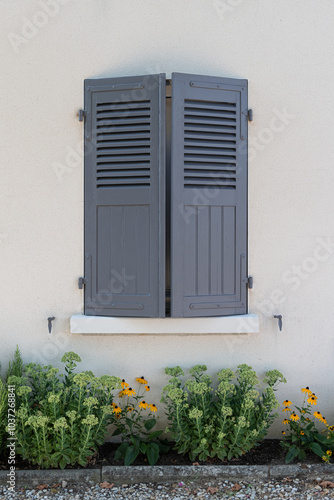 Volets fermés devant un parterre de fleur