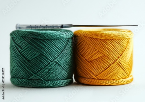 Spools of green and yellow thread with a sewing needle on a light background in a crafting workspace photo