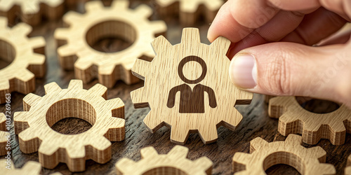 A wooden gear puzzle with a human icon being assembled by a hand, representing teamwork, collaboration, and organizational synergy in business and personal development. photo