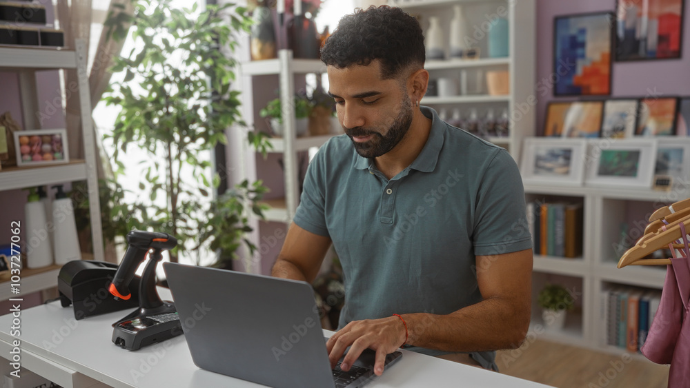 Obraz premium Young man working on a laptop in a home decor store, surrounded by various decorations and indoor plants.