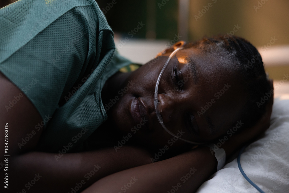 African patient resting in a hospital bed, connected to an oxygen supply, while calmly looking towards the camera. African patient resting in a hospital bed, connected to an oxygen supply, while calmly looking towards the camera.