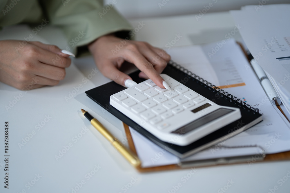 Close-up of a Hand Using a Calculator:  A businesswoman's hand, adorned with elegant nails, confidently presses buttons on a white calculator, surrounded by paperwork.