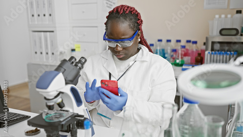 A focused african woman scientist with braids analyzes data on her phone in a modern laboratory