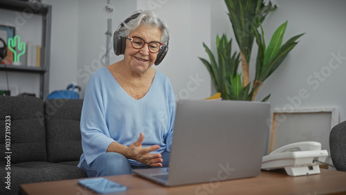 Senior woman with glasses and headphones using laptop in a cozy living room.