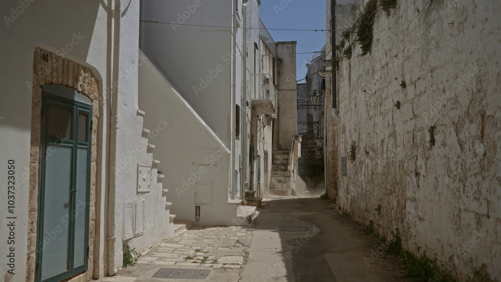 Scenic narrow alley with whitewashed buildings in ostuni, puglia, italy, featuring iconic stone walls, steps, and a clear blue sky. Scenic narrow alley with whitewashed buildings in ostuni, puglia, italy, featuring iconic stone walls, steps, and a clear blue sky.