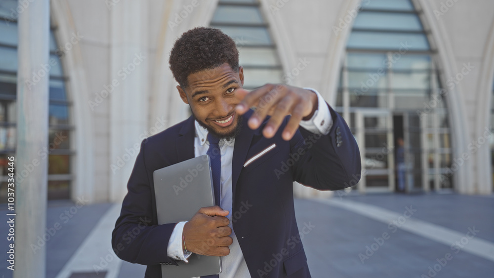 Handsome young man smiling outdoors while holding a laptop on an urban street with modern buildings in the background. Handsome young man smiling outdoors while holding a laptop on an urban street with modern buildings in the background.