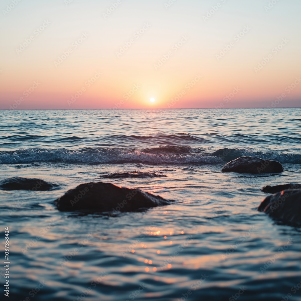 Obraz premium Ocean waves softly break against the rocks under a colorful sky at sunset, evoking a sense of peace.