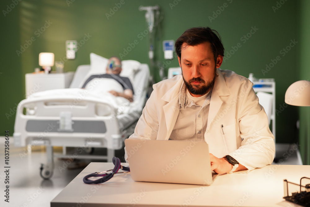 A middle-aged doctor sits tiredly at his desk in a hospital room. An overtired doctor at work A middle-aged doctor sits tiredly at his desk in a hospital room. An overtired doctor at work