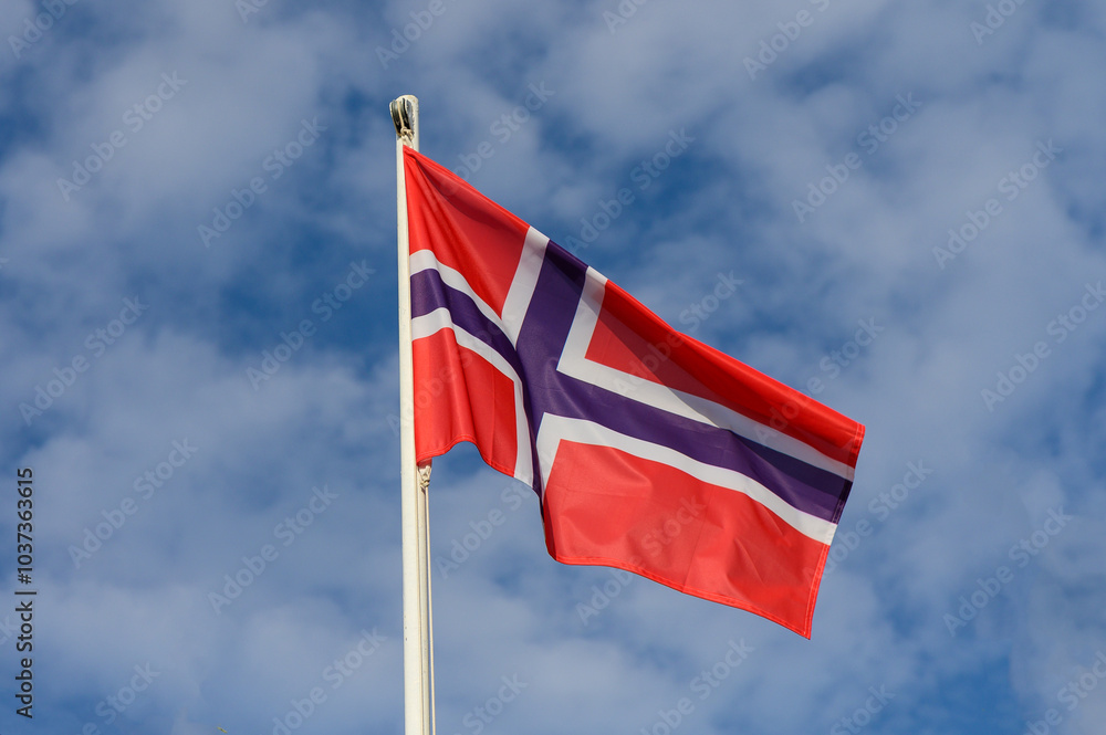 Norwegian flag proudly waving under a bright blue sky with fluffy clouds during a sunny day in Norway Norwegian flag proudly waving under a bright blue sky with fluffy clouds during a sunny day in Norway