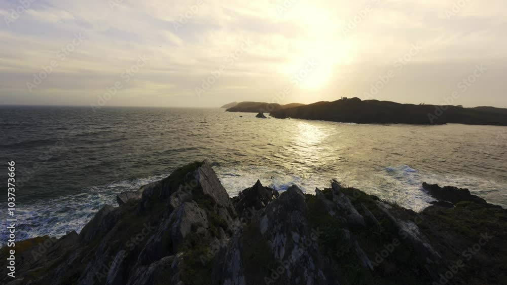 Watch the stunning sunset casting golden hues over the ocean waves as they crash against rugged coastal cliffs. Distant islands are visible in this picturesque setting. Watch the stunning sunset casting golden hues over the ocean waves as they crash against rugged coastal cliffs. Distant islands are visible in this picturesque setting.