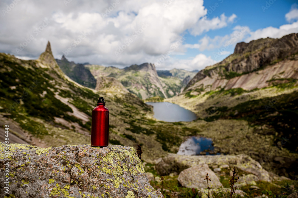 a red tourist bottle in the mountains on the background of a beautiful lake a red tourist bottle in the mountains on the background of a beautiful lake
