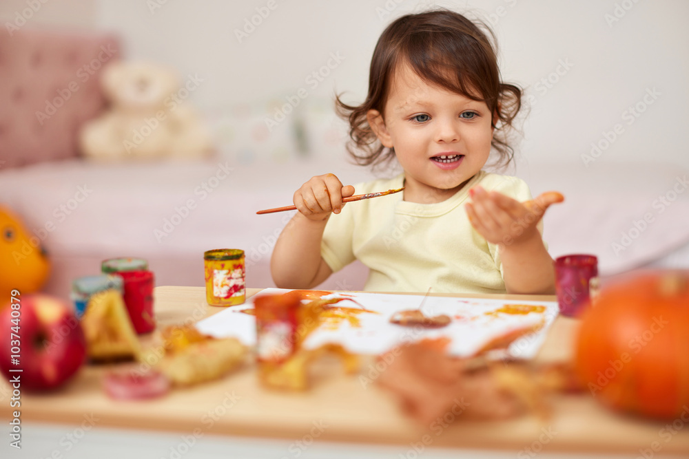 smiling little child girl painting her hands and autumn leaves. baby girl drawing hands in yellow paint smiling little child girl painting her hands and autumn leaves. baby girl drawing hands in yellow paint