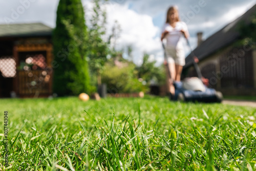 This image captures someone mowing their lawn with a push lawn mower. The person is holding onto the handle, guiding the mower over a well-maintained grassy area. photo