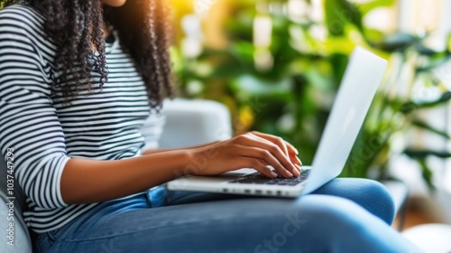 A woman sits comfortably on a couch, focused on her laptop as sunlight filters through nearby plants, creating a warm and inviting atmosphere perfect for productivity