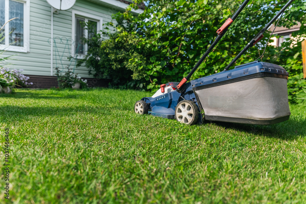 A lawn mower is cutting green grass, the gardener with a lawn mower is working in the backyard, a side view. A lawn mower is cutting green grass, the gardener with a lawn mower is working in the backyard, a side view.