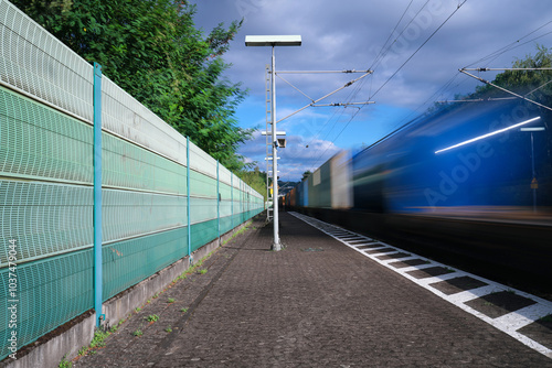 Lärmschutzwand an Bahnstrecke zur Reduzierung von Bahnlärm und vorbeifahrender Güterzug - Stockfoto