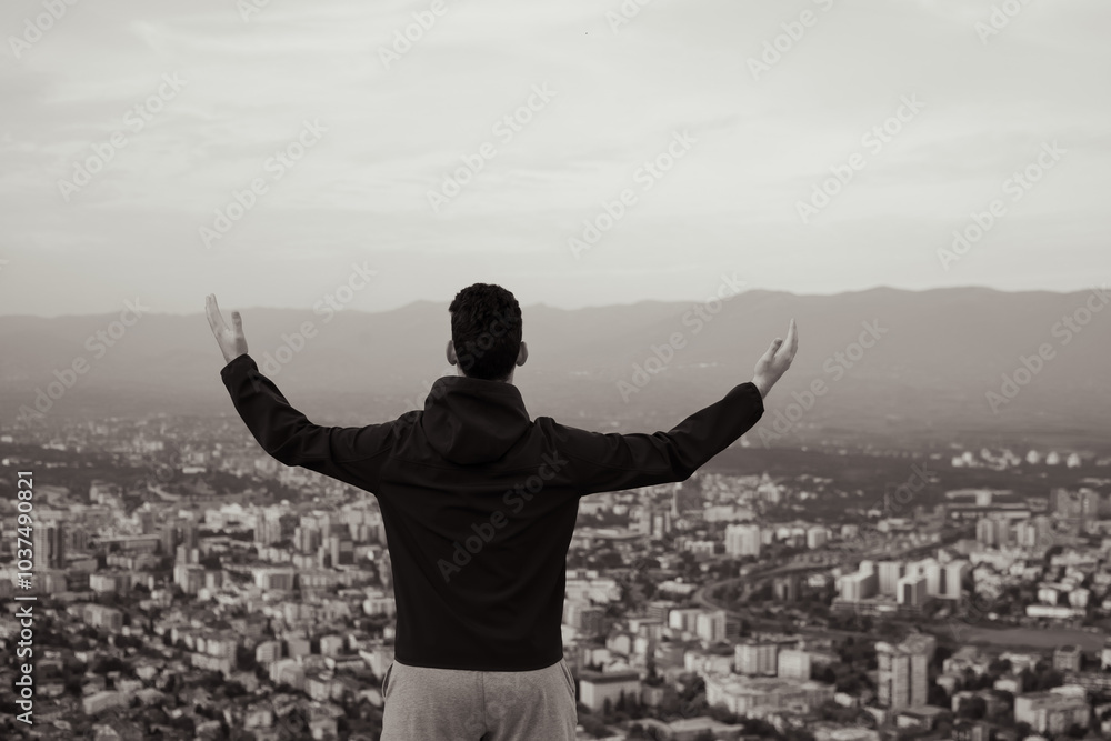 Rear portrait of an excited man raising his arms in nature, looking towards the city and embracing freedom. Rear portrait of an excited man raising his arms in nature, looking towards the city and embracing freedom.