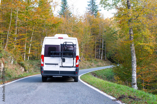 a white camper van on a road route through a beech forest with colorful trees in autumn. Concept: Camper life, freedom and adventure. picturesque destinations, Irati Forest Spain