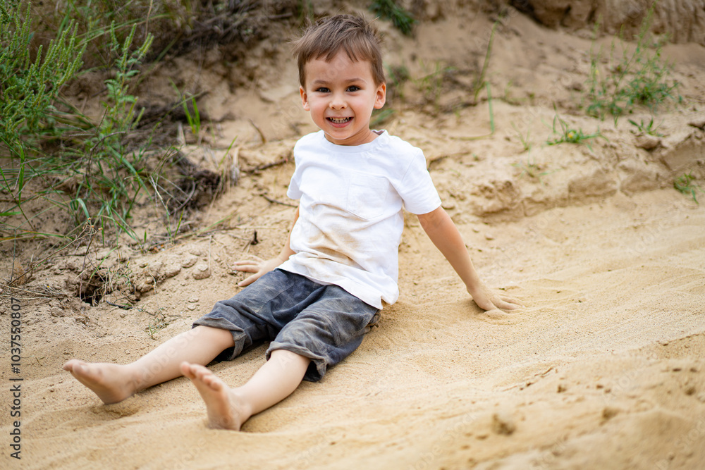 Young boy playing happily in soft sand outdoors. A child sits in the sand, smiling broadly as he enjoys a sunny day at the beach, making the most of outdoor playtime. Young boy playing happily in soft sand outdoors. A child sits in the sand, smiling broadly as he enjoys a sunny day at the beach, making the most of outdoor playtime.