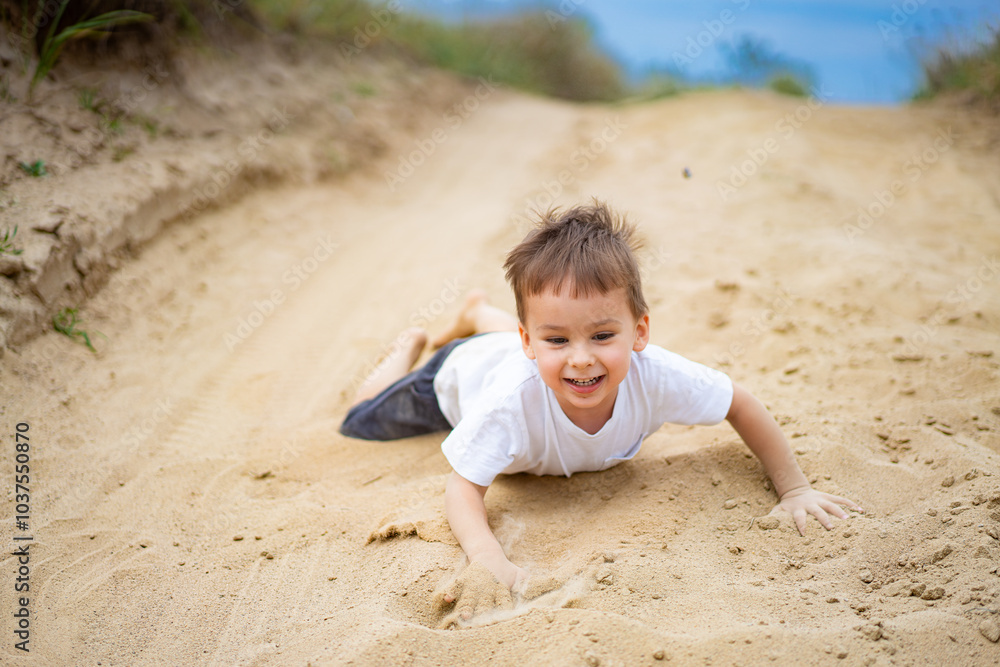 Happy child playing in the sand on a country road. A joyful boy enjoys crawling through sandy ground on a sunny day, exploring his surroundings with a big smile on his face. Happy child playing in the sand on a country road. A joyful boy enjoys crawling through sandy ground on a sunny day, exploring his surroundings with a big smile on his face.