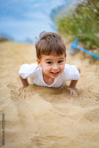 Boy playing in sand by the water. A joyful young boy crawls through the soft sand by the water, enjoying a sunny day outdoors and embracing playful activities.