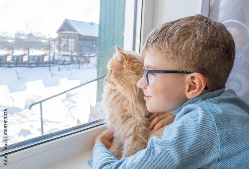 Beautiful scene two friends looking out fo window. Small boy with a cat stares out of window watching falling snow, focus on cat