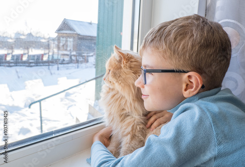 Obraz na płótnie Beautiful scene two friends looking out fo window. Small boy with a cat stares out of window watching falling snow, focus on cat w salonie