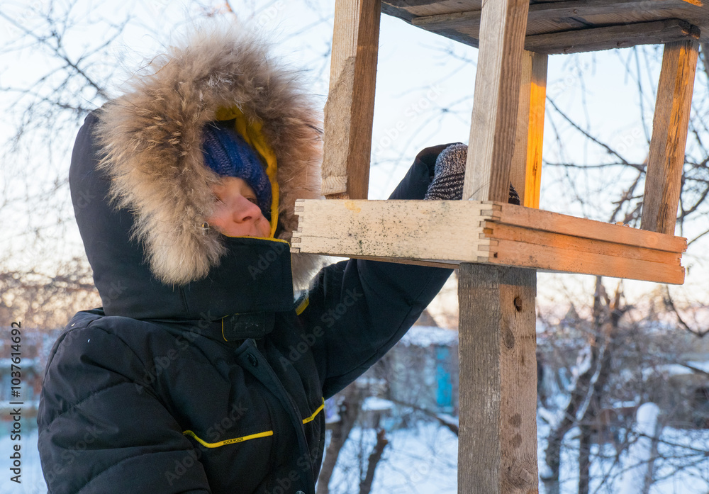 Adorable child, boy feeding birds on a cold winter day, pouring grain into a feeder. A child helps birds in winter. Winter activities for children.