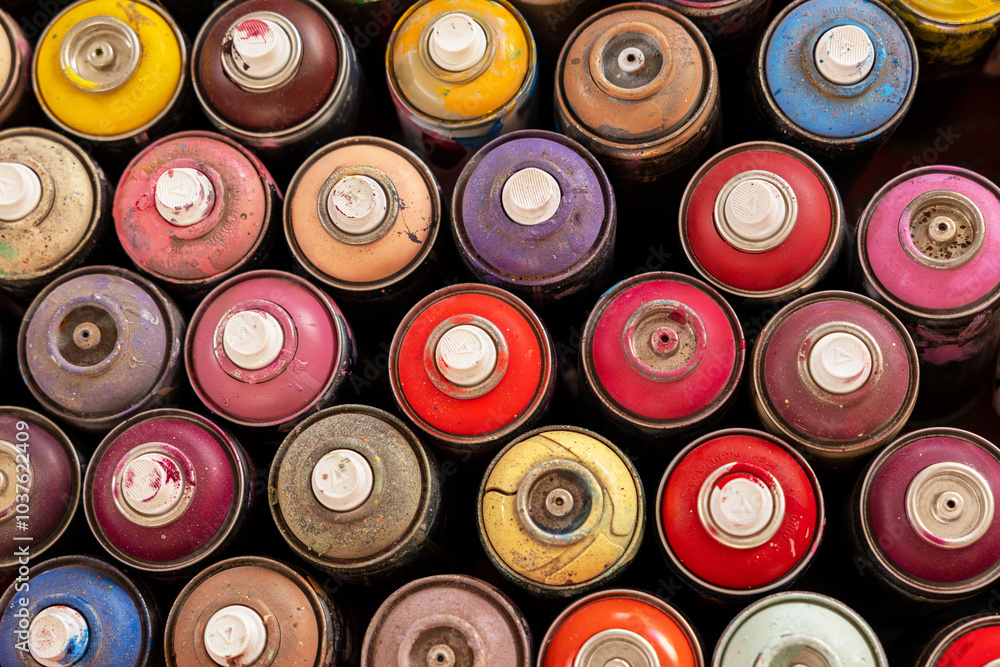 Top view of a collection of colorful spray paint cans, showcasing various vibrant shades, textures, and worn surfaces, ideal for art projects.. Top view of a collection of colorful spray paint cans, showcasing various vibrant shades, textures, and worn surfaces, ideal for art projects..
