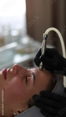 Professional dermatologist in medical gloves performs microdermabrasion on woman in a beauty salon