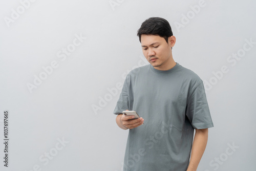 Sad and disappointed expression of adult Asian man using mobile phone with casual t-shirt isolated on white background
