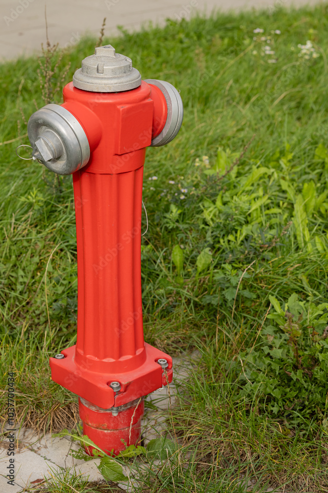 Bright red fire hydrant standing in green grass near a sidewalk on a sunny day. Concept of urban safety, emergency equipment, and public infrastructure in a city environment Bright red fire hydrant standing in green grass near a sidewalk on a sunny day. Concept of urban safety, emergency equipment, and public infrastructure in a city environment