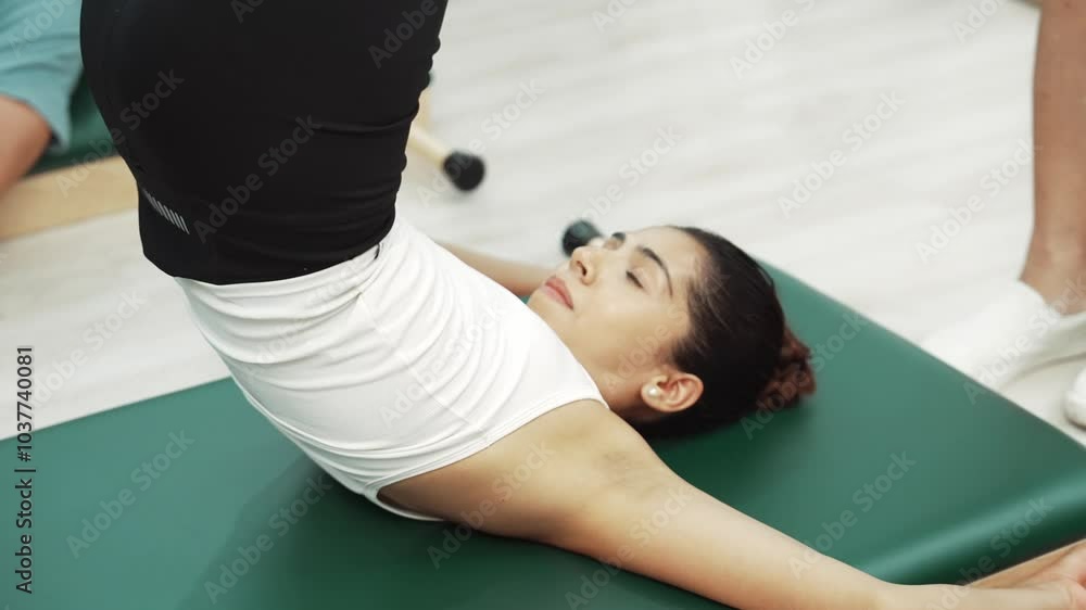 Pilates client practicing leg raises with core engagement during a Pilates session. Woman pose at reverse crunch while trainer helping for strengthen abdominal and improving flexibility. Habituate. Pilates client practicing leg raises with core engagement during a Pilates session. Woman pose at reverse crunch while trainer helping for strengthen abdominal and improving flexibility. Habituate.
