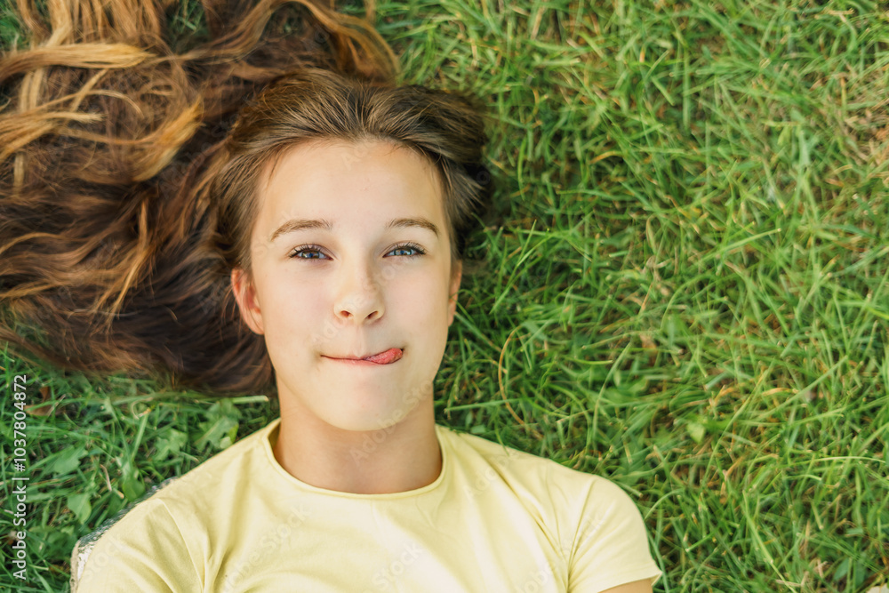 little girl licking her lips and sticking out tongue on natural green grass background, hungry child sticking out tasty gesture little girl licking her lips and sticking out tongue on natural green grass background, hungry child sticking out tasty gesture