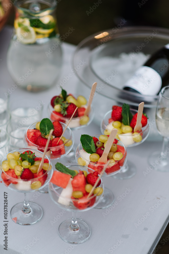 A beautifully arranged table is adorned with a selection of glasses that are filled with an array of colorful fruit and a bottle of champagne sitting elegantly beside them A beautifully arranged table is adorned with a selection of glasses that are filled with an array of colorful fruit and a bottle of champagne sitting elegantly beside them