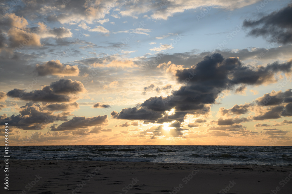 Obraz premium As the sun gently descends toward the horizon, the picturesque ocean reflects the vibrant hues of the clouds in the sky above