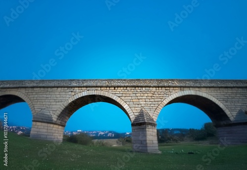 Stone arch bridge with a blue sky background, grass in the foreground.