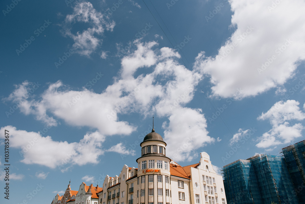 Fototapeta premium A large, impressive building featuring a tall tower located on its rooftop, beautifully set against a clear blue sky scattered with white clouds