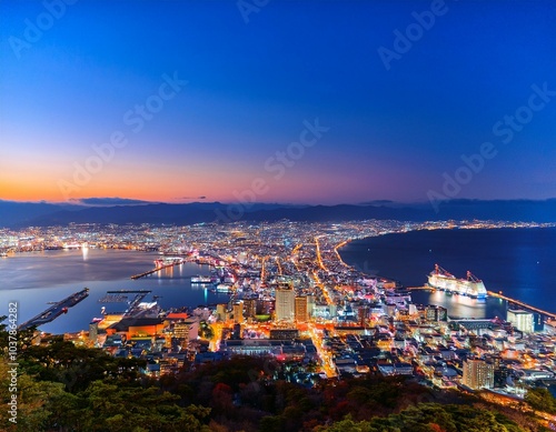 函館山から見下ろす、世界三大夜景のひとつとされる函館の夜景。湾に沿って広がる街の光が宝石のように輝き、港に停泊する船の灯りも穏やかに瞬いている。ロマンチックな夜景を眺めるカップルや観光 photo