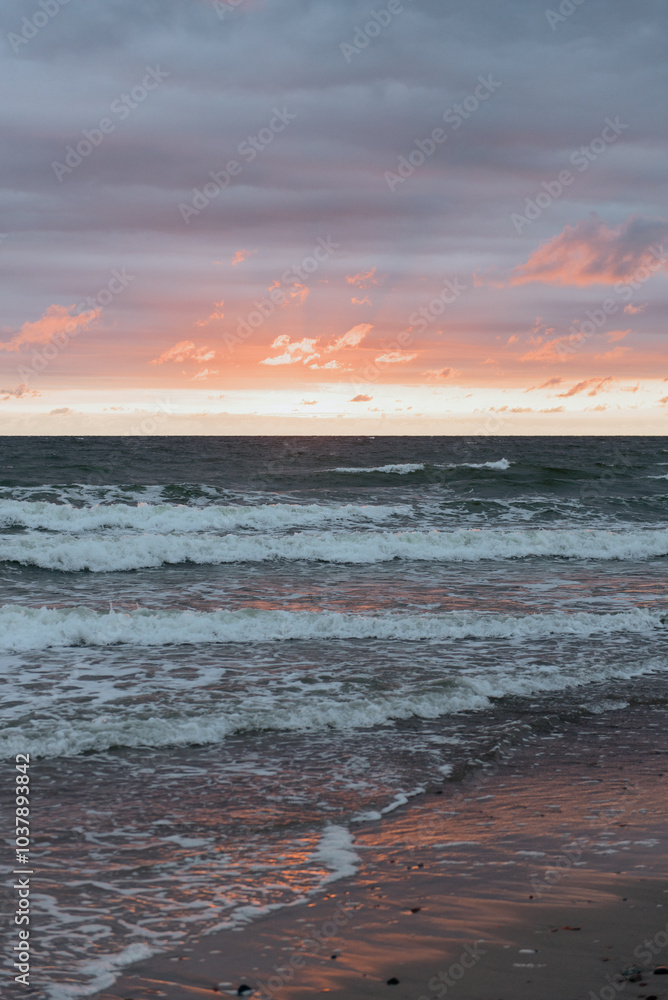 Obraz premium A breathtaking sunset over the vast ocean, where waves are continuously crashing onto the sandy beach, creating a peaceful atmosphere