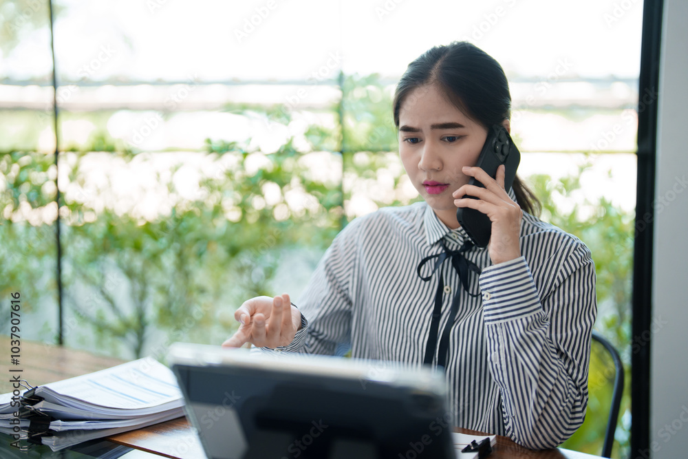 A young woman is sitting at her desk, talking on the phone while gesturing with her hand. She appears to be discussing something important A young woman is sitting at her desk, talking on the phone while gesturing with her hand. She appears to be discussing something important