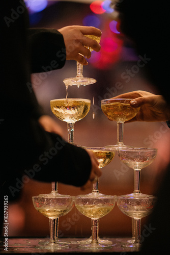 People celebrating by pouring champagne into a beautifully arranged pyramid of glassware that creates a stunning visual display of drinks