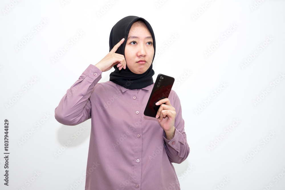 Portrait of Asian, Indonesian woman wearing shirt, hijab and holding mobile phone who is overwhelmed with emotions and bad thoughts, unhappy and stressed. Isolated on white background Portrait of Asian, Indonesian woman wearing shirt, hijab and holding mobile phone who is overwhelmed with emotions and bad thoughts, unhappy and stressed. Isolated on white background