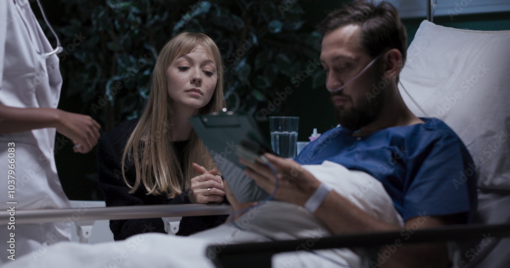 Man signs medical consent forms while being supported by a young woman sitting beside him. Man signs medical consent forms while being supported by a young woman sitting beside him.
