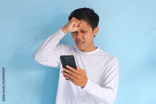 Young Asian man holding his mobile phone with sad expression  photo