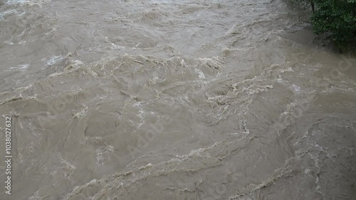 The river swollen after heavy rainfall and floodwater crashing through valley. The water flows fast from the high valley to the plain. General contest of a river in flood